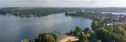 Luftaufnahme von Ratzeburg am Ratzeburger See mit Badestelle, Bootsstegen und bewaldeten Ufern. - zum Artikel 'Sommerausflug nach Ratzeburg: Zwischen Rudersport und Backsteingeschichte'