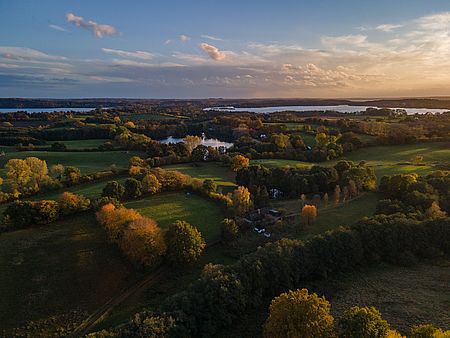 Luftaufnahme der Holsteinischen Schweiz mit grünen Feldern, herbstlich gefärbten Wäldern und mehreren Seen im warmen Licht der tief stehenden Sonne.