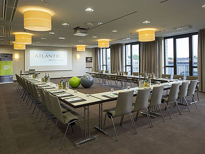 Tagungsraum des Atlantic Hotels Lübeck. Die Bestuhlung ist in U-Form eingerichtet mit Blick auf eine Leinwand.