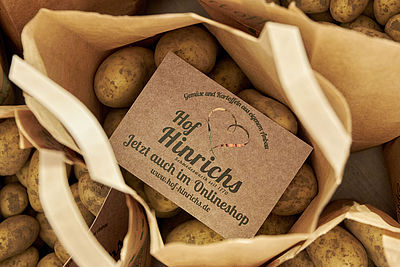 Verschiedene Tüten, die mit Kartoffeln gefüllt sind. In einer Tüte liegt eine Karte mit Werbung für den Hof Hinrichs und den Onlineshop.
