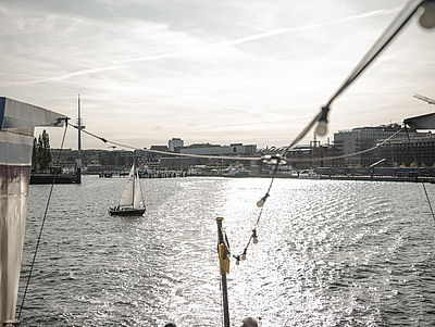Blick auf die Kieler Förde mit Segelboot im Vordergrund und Stadt im Hintergrund.