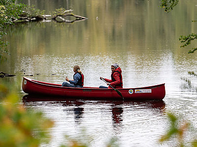 Zwei Personen fahren mit einem roten Kanu über einen kleinen Kanal.