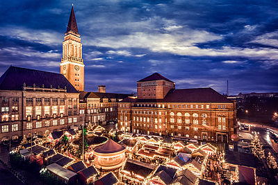 Kleine weihnachtliche Hütten stehen auf dem Kieler Weihnachtsmarkt. Im Hintergrund befindet sich der Rathausturm.