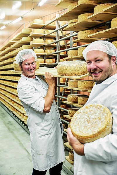 Zwei Männer stehen in einem Käselager. 