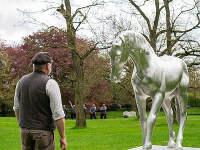 Mann steht bei einer Kunstausstellung vor einem silbernen Pferd