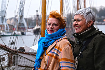 Zwei ältere Frauen stehen am Wasser vor einem Segelschiff.