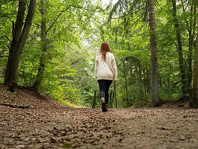 Eine Frau geht auf einem von Laub bedeckten Waldweg durch die grüne Hahnheide.