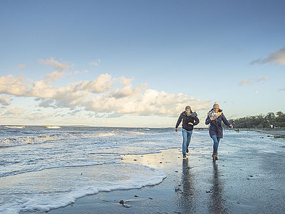 Ein Mann und eine Frau spazieren in winterlicher Kleidung entlang der Ostsee.