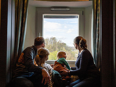 Familie sitzt vor einem Fenster in einer Unterkunft