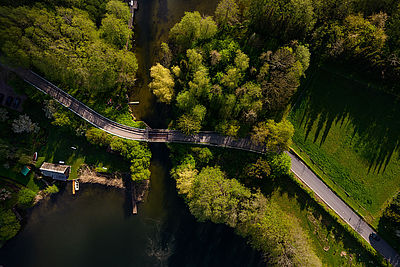 Ein Radweg befindet sich zwischen grüner Vegetation und überquert mit einer Brücke ein Gewässer.