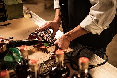Eine Person bringt ein Etikett auf einer Flasche an; weitere verschlossene Flaschen stehen im Vordergrund.
