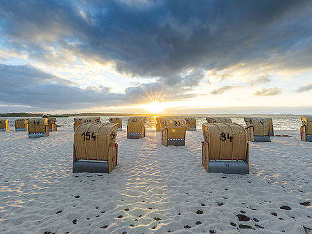 Strandkörbe stehen auf dem Sandstrand. Die Sonne steht tief über der Ostsee.