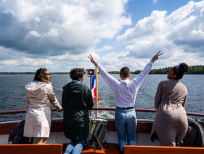 Vier Menschen stehen auf einem Boot mit Blick aufs Wasser.