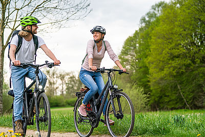 Ein Mann und eine Frau fahren Fahrrad. Sie sind sommerlich gekleidet und tragen Fahrradhelme.