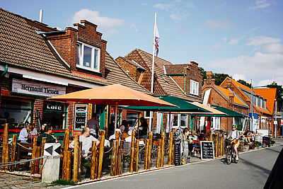 Der Außenbereich des Schiffercafés in Kiel ist gut besucht, während eine Radfahrerin vorbeifährt.