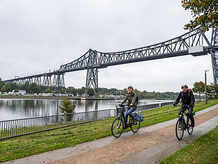 Ein Mann und eine Frau fahren mit ihren Fahrrädern unter der Eisenbahnhochbrücke Rendsburg hindurch.