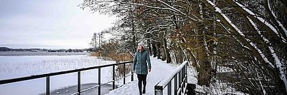 Eine junge Frau geht über eine kleine Brücke am Großen Segeberger See. Die Landschaft wurde von einer Schneedecke bedeckt. - zum Artikel 'Mehr als Kalkberg und Karl May: Bad Segeberg'
